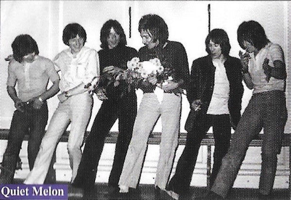 B/w image of the band Quiet Melon. Six band members standing in line with their right legs extended. Rod Stewart is hilding a bunch of flowers.