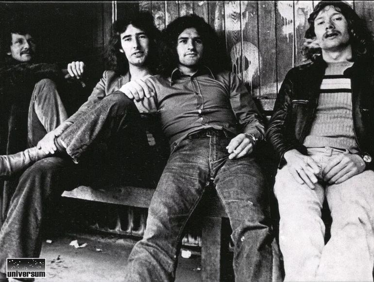 Black & white image of Plymouth based band, Stonehouse, lounging around in what looks like a wooden, graffiti spattered bus shelter.